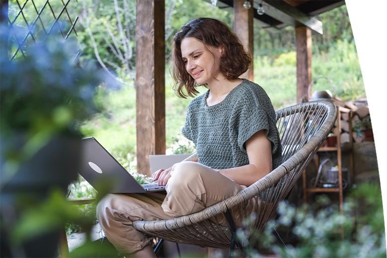 Young adult Caucasian woman sitting on cottage terrace using laptop